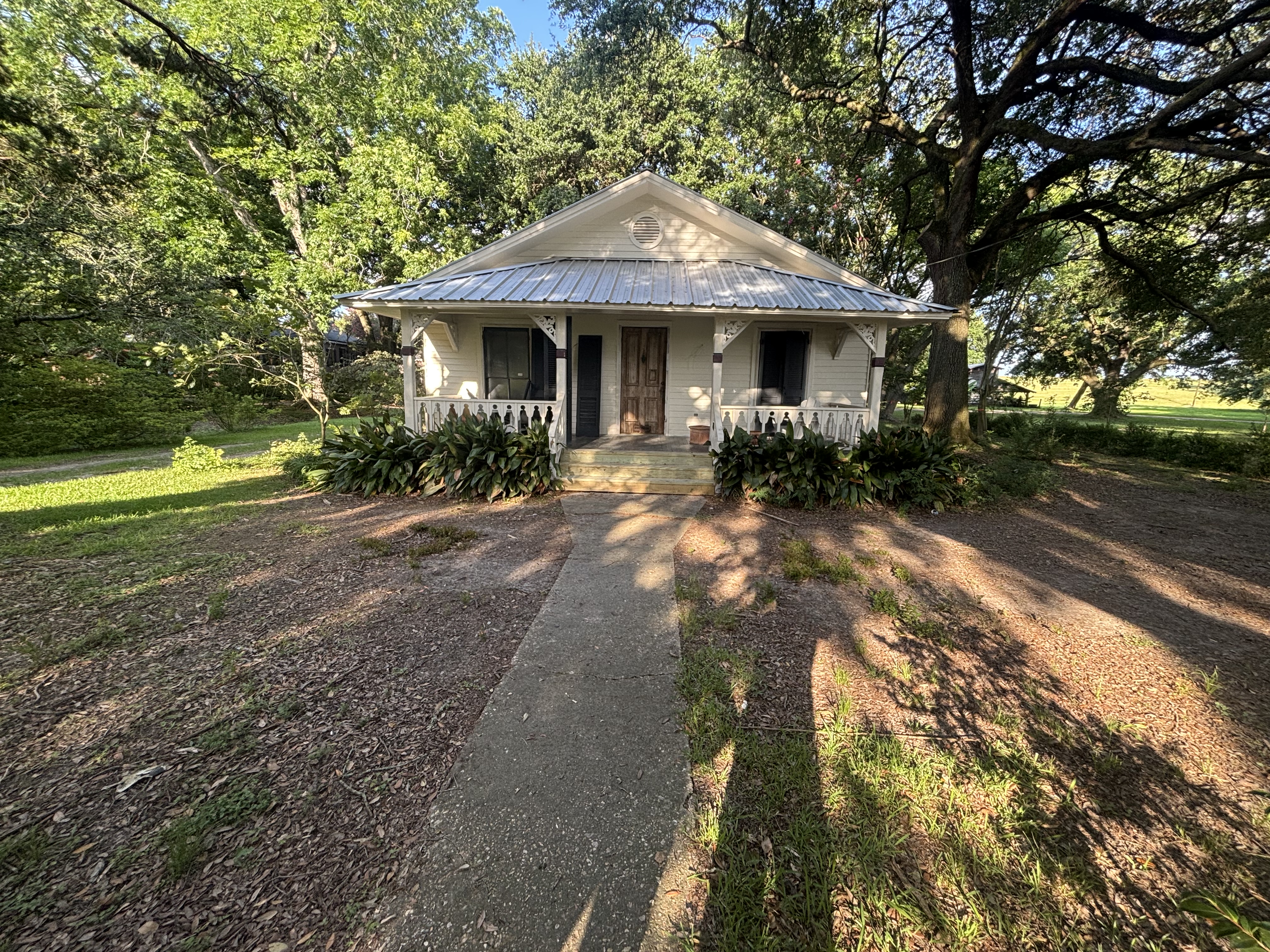 Before - cottage with bare dirt yard, weeds, and aging concrete walkway, no landscape beds