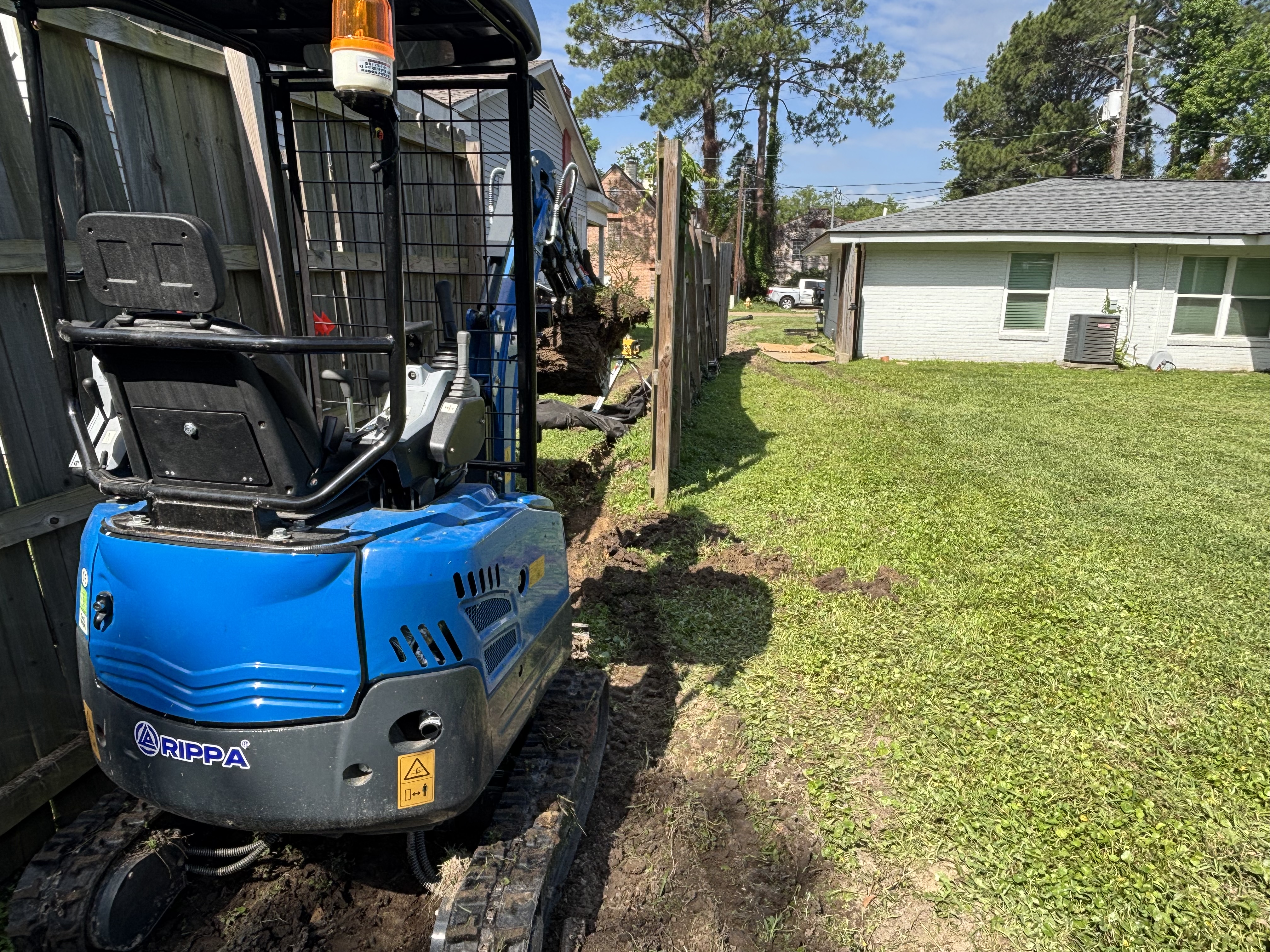 Mini excavator trenching for French drain installation in Baton Rouge residential yard