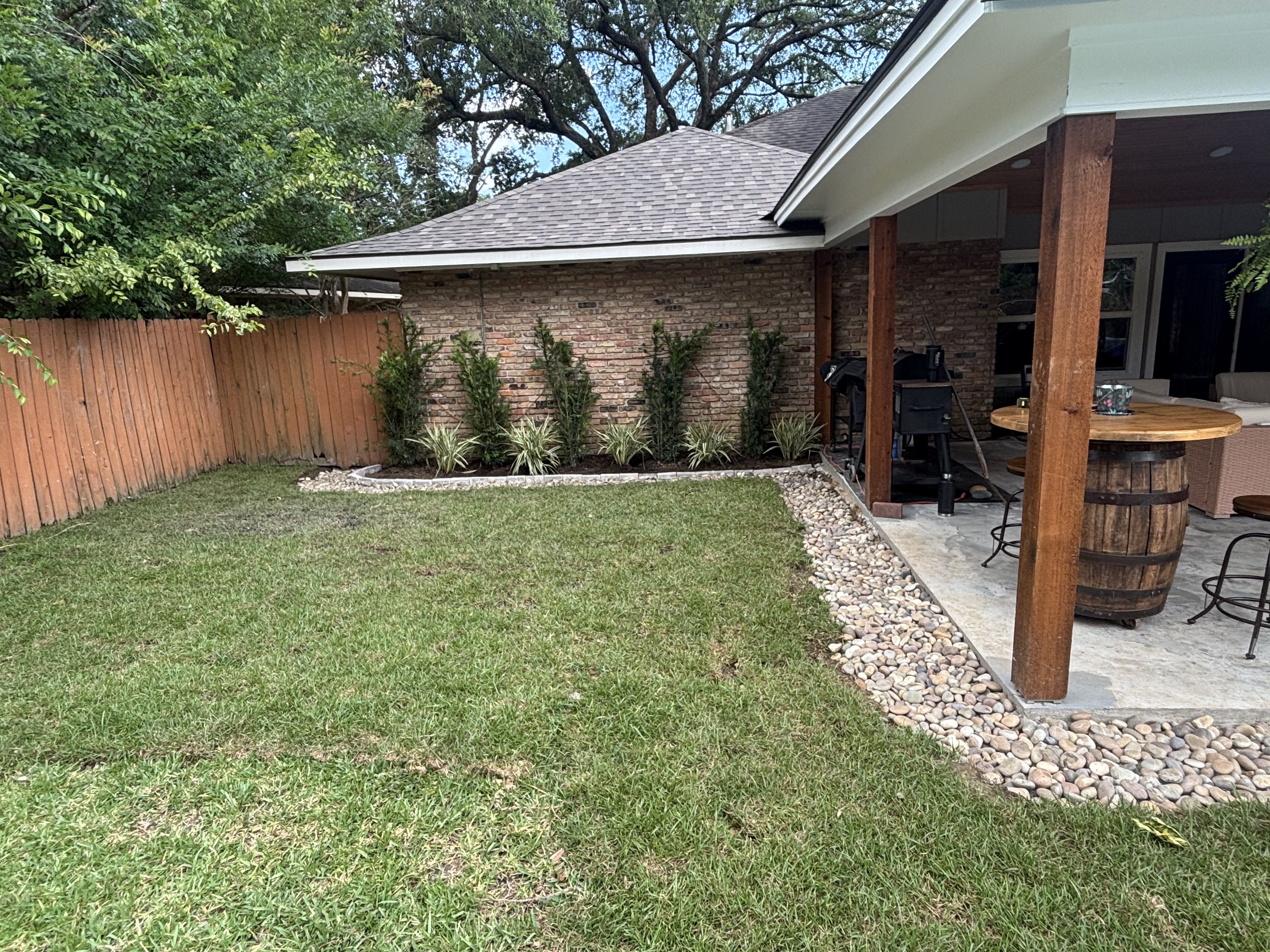 Open French drain with river rock border along patio edge, new landscape beds and sod - Baton Rouge drainage and landscaping